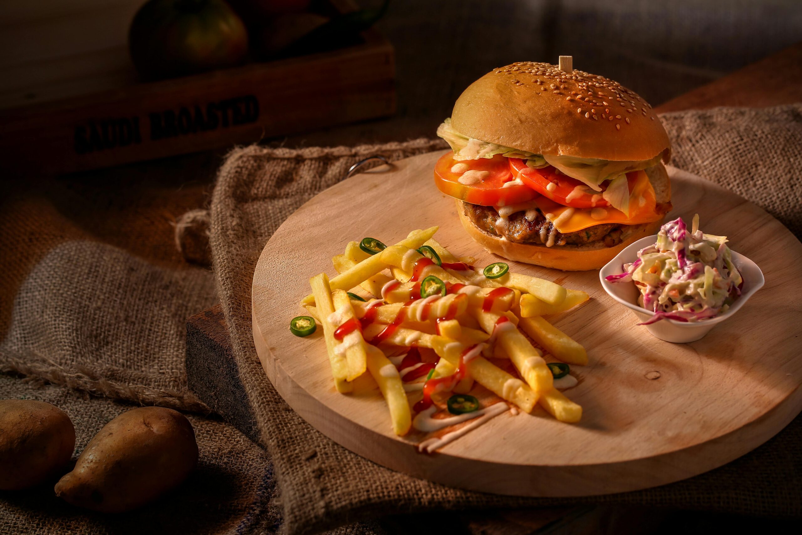 A mouthwatering cheeseburger with fresh fries and coleslaw on a rustic wooden board.